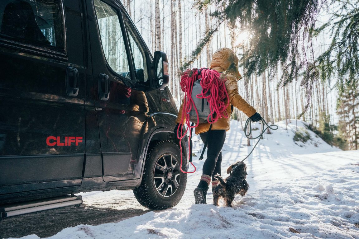Anna Laitinen ja pieni koira kävelevät metsässä lumihangessa matkailuauton ohi.
